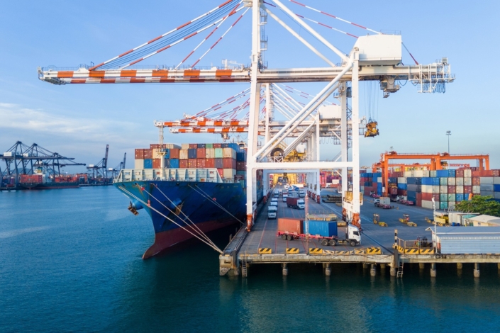 gantry cranes loading cargo container ship at a busy commercial port terminal, with trailer trucks lined up on the dock to support global maritime logistics and supply chain operations.